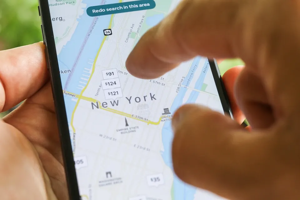 Close-up of hand using smartphone to search New York City map on Airbnb app.